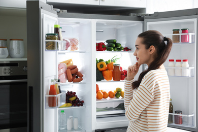 Photo of Beautiful young woman near open refrigerator in kitchen