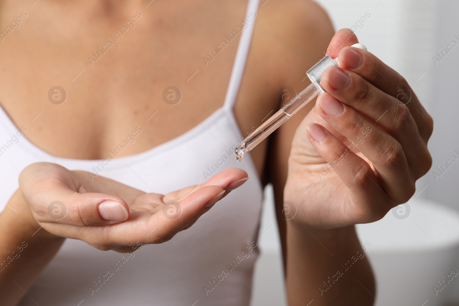 Photo of Woman applying cosmetic serum onto her finger on light background, closeup