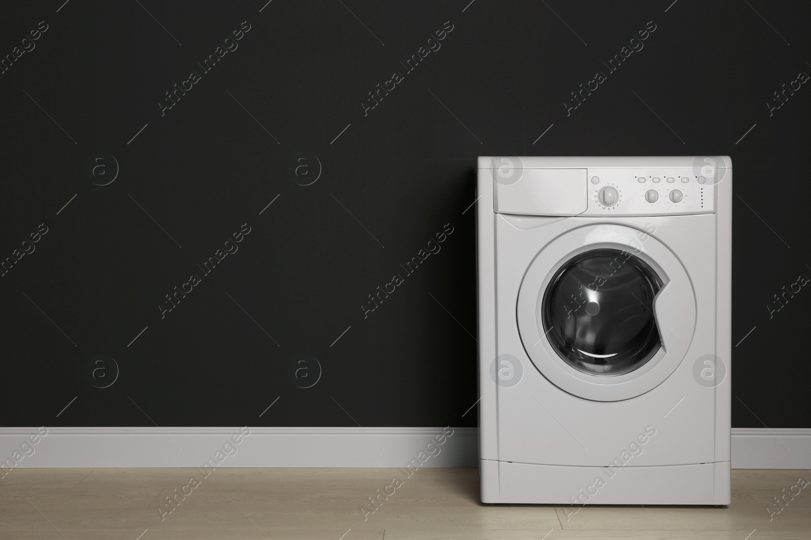 Photo of Modern washing machine near black wall, space for text. Laundry day