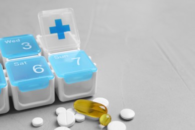 Weekly pill box with medicaments on grey table, closeup. Space for text