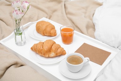 Photo of Tray with tasty croissants, drinks and flowers on bed
