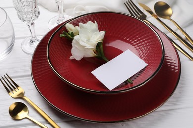 Stylish table setting. Dishes, cutlery, blank card and flower on white wooden background, closeup