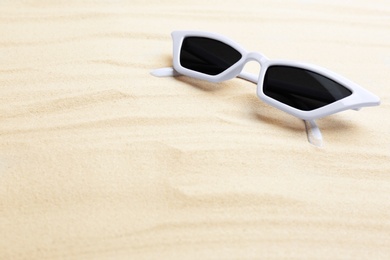 Stylish sunglasses on white sand, space for text. Summer time