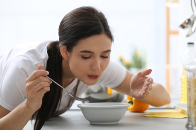 Photo of Young woman eating tasty vegetable soup at countertop in kitchen