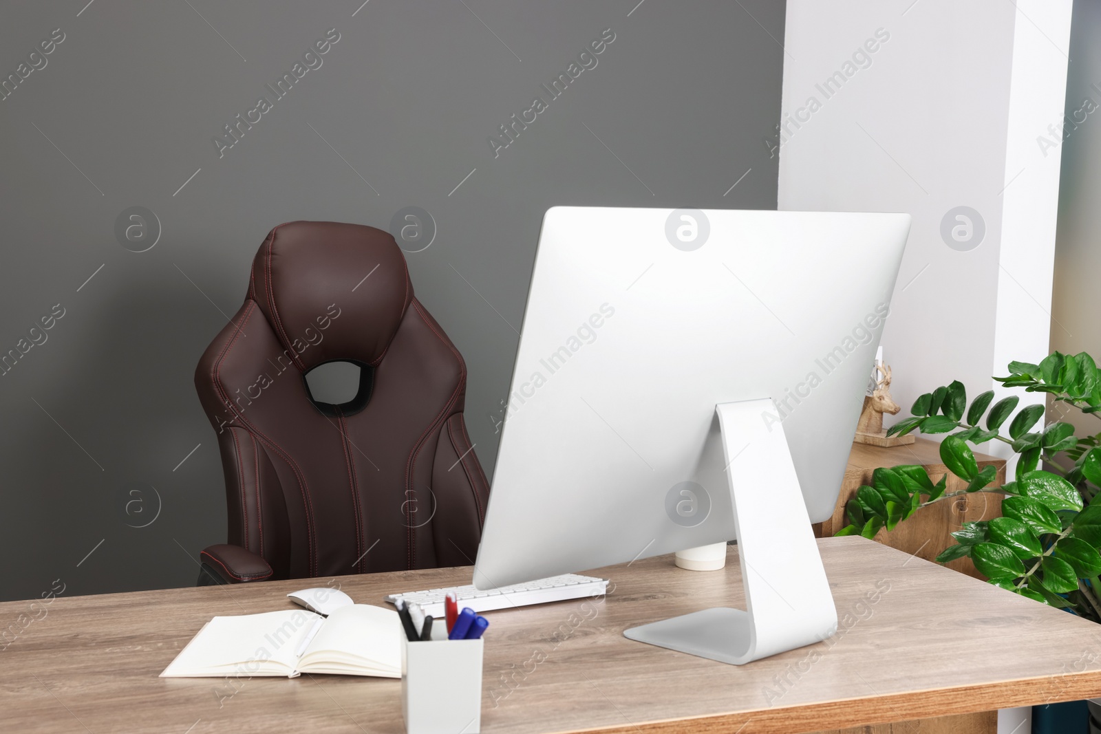 Photo of Computer, notebook and stationery on table near chair in office. Boss workplace