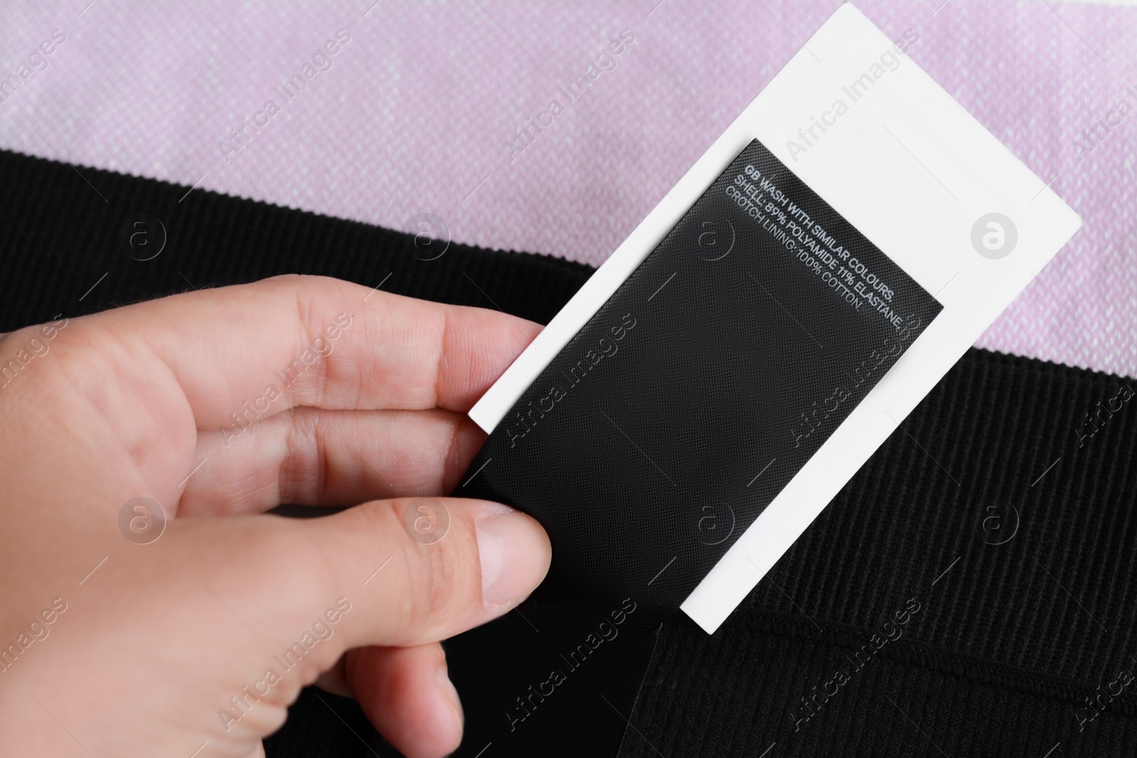 Photo of Woman holding clothing label on black garment, closeup