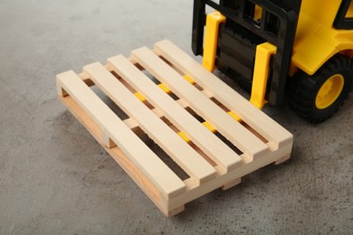 Toy forklift with wooden pallet on light grey table, closeup