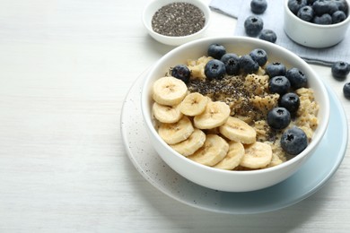 Photo of Tasty oatmeal with banana, blueberries and chia seeds served in bowl on white wooden table, space for text