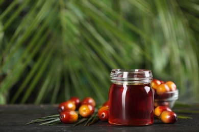 Image of Palm oil in glass jar, tropical leaf and fruits on wooden table. Space for text