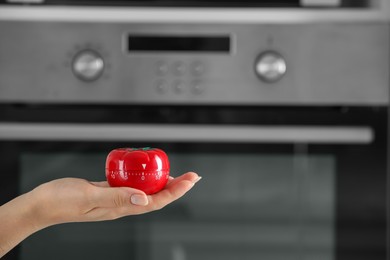 Photo of Woman holding kitchen timer in shape of tomato near oven, closeup. Space for text