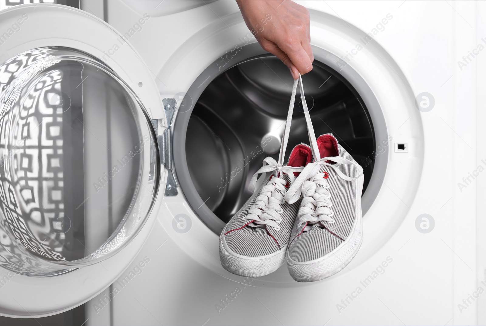 Photo of Woman putting pair of sport shoes into washing machine, closeup