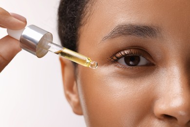 Woman applying serum onto her face on white background, closeup