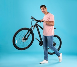 Handsome young man with modern bicycle on light blue background