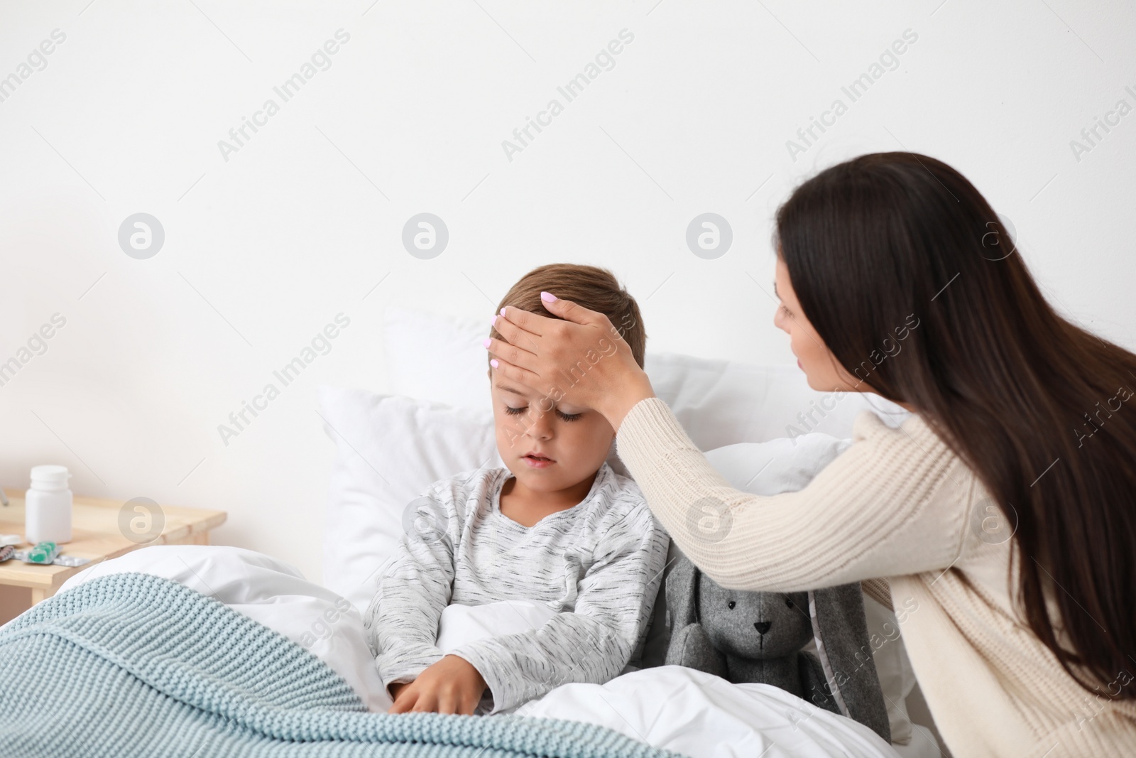 Photo of Mother taking care of her little son suffering from cold in bed, space for text