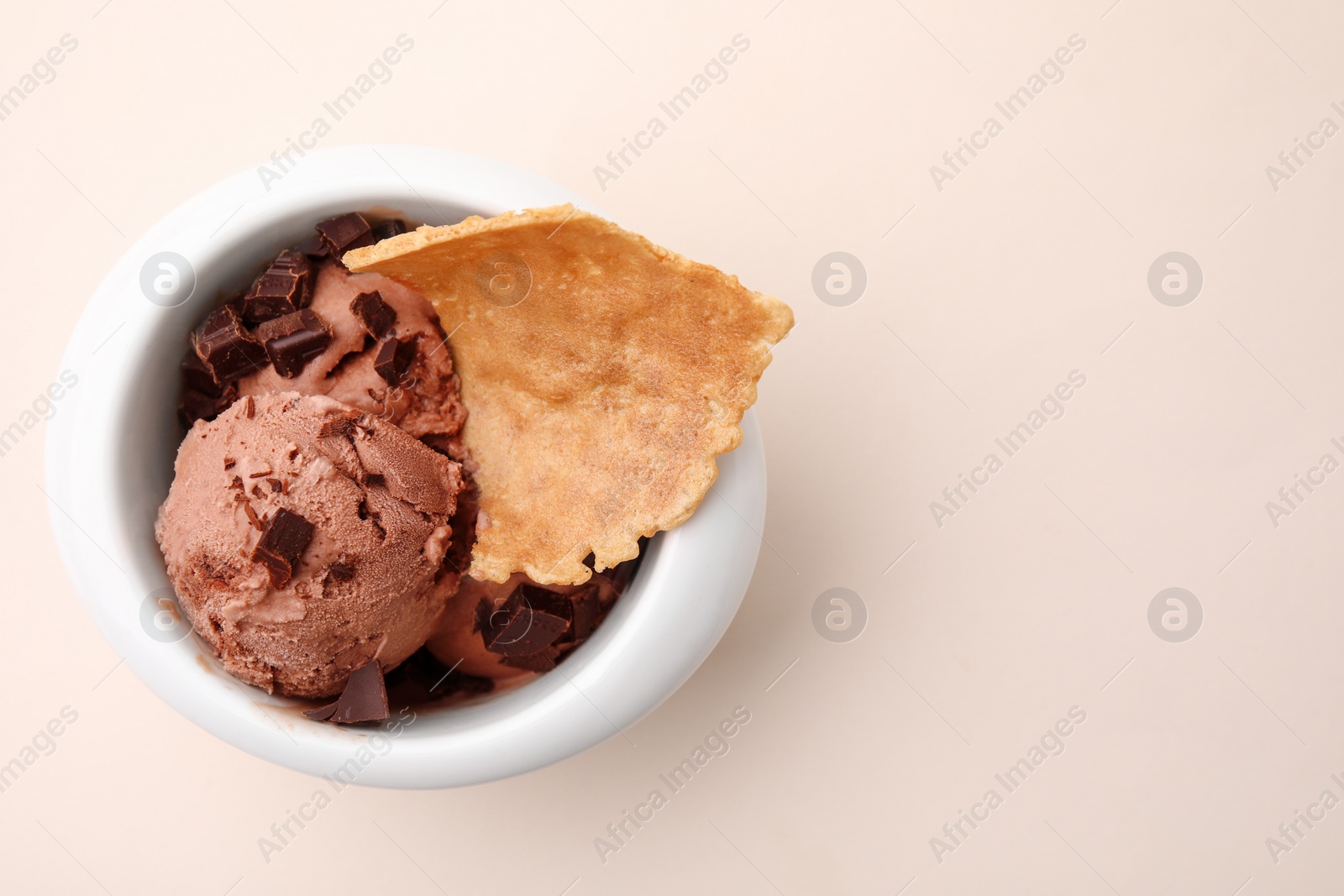 Photo of Tasty chocolate ice cream and piece of waffle cone in bowl on beige background, top view. Space for text