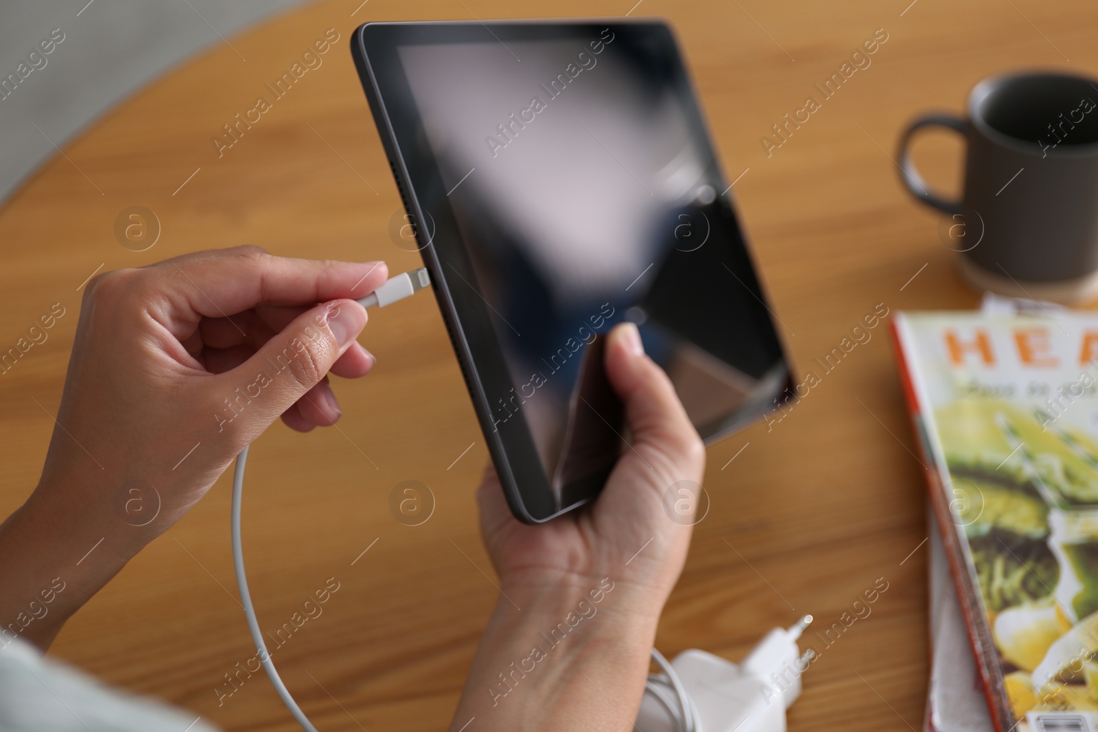 Photo of Woman connecting charger cable to tablet at wooden table, closeup