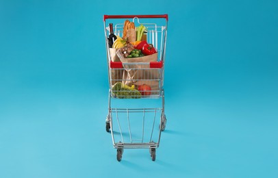 Shopping cart full of groceries on light blue background