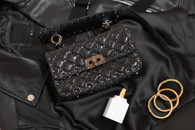 Photo of Leather bag, bottle of perfume and golden bracelets on black fabric, flat lay