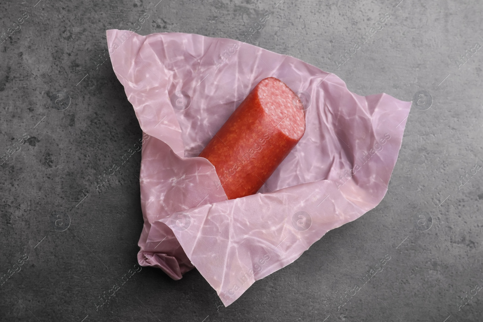 Photo of Fresh tasty sausage in beeswax food wrap on grey table, top view