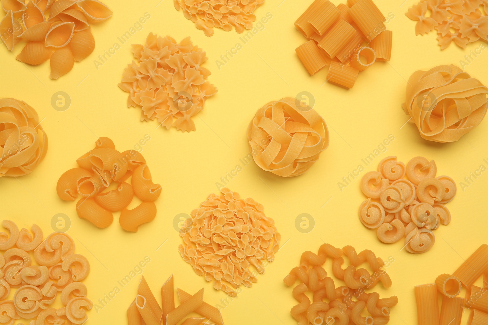 Photo of Different types of pasta on yellow background, flat lay