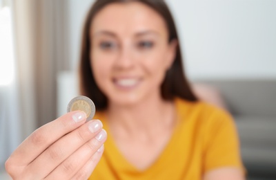 Photo of Young woman holding coin at home, focus on hand