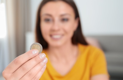 Young woman holding coin at home, focus on hand