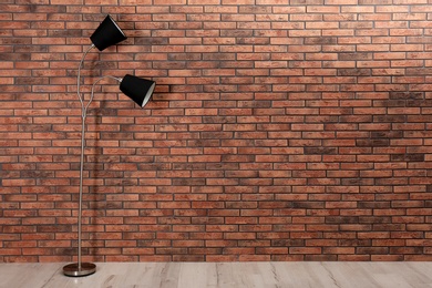 Photo of Stylish lamp on floor near brick wall. Space for text