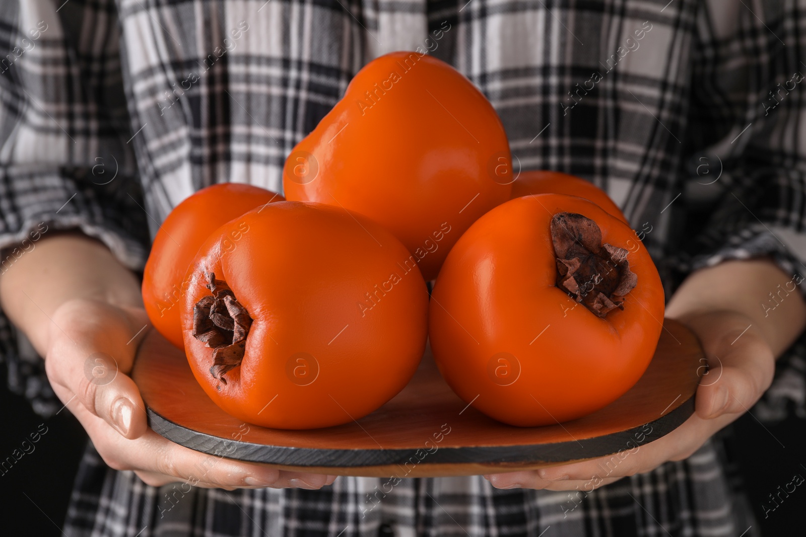 Photo of Woman holding delicious ripe juicy persimmons, closeup