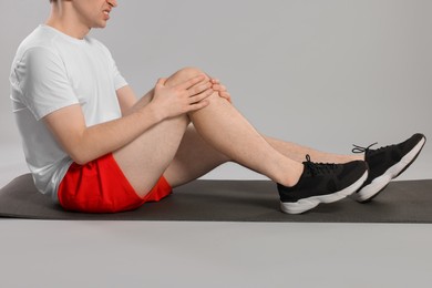Man suffering from leg pain on mat against grey background, closeup