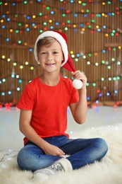 Cute little child in Santa hat on blurred lights background. Christmas celebration