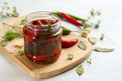 Glass jar of pickled chili peppers and ingredients on white table. Space for text