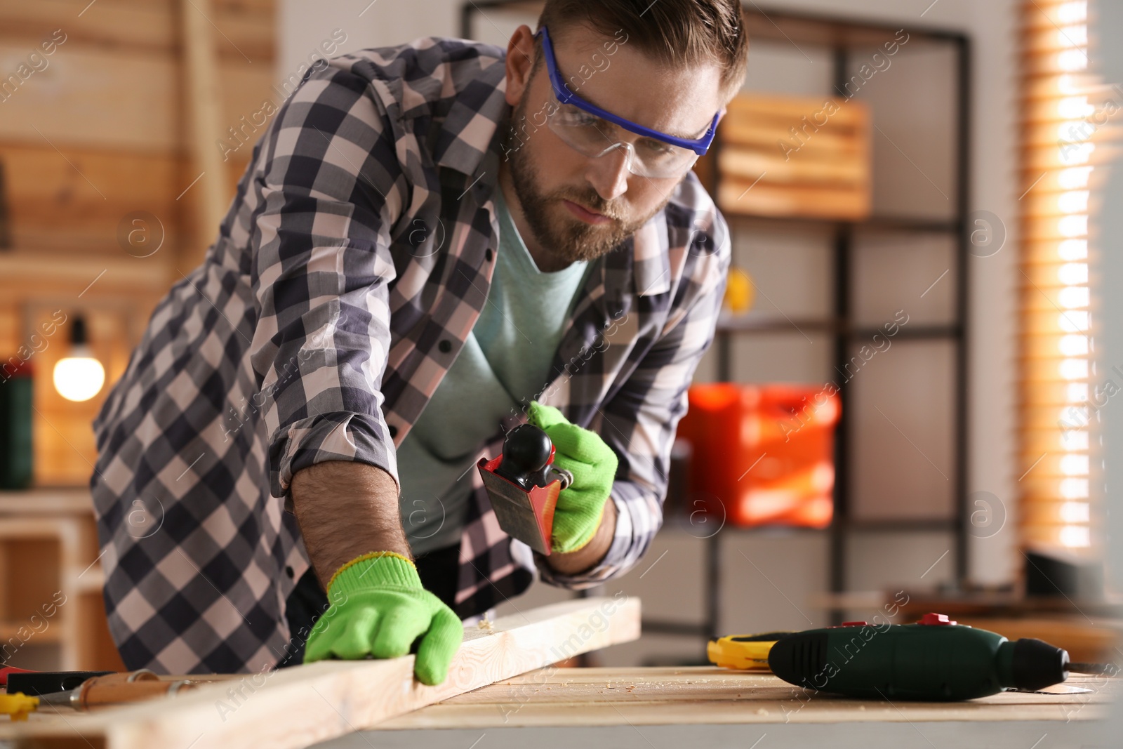 Photo of Carpenter shaping wooden bar with hand plane at table in workshop