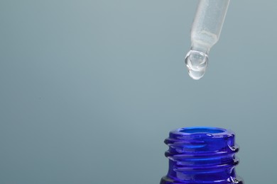 Dripping serum from pipette into bottle on grey background, closeup. Space for text