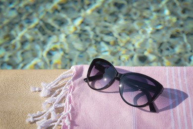 Photo of Stylish sunglasses and blanket near outdoor pool on sunny day, space for text