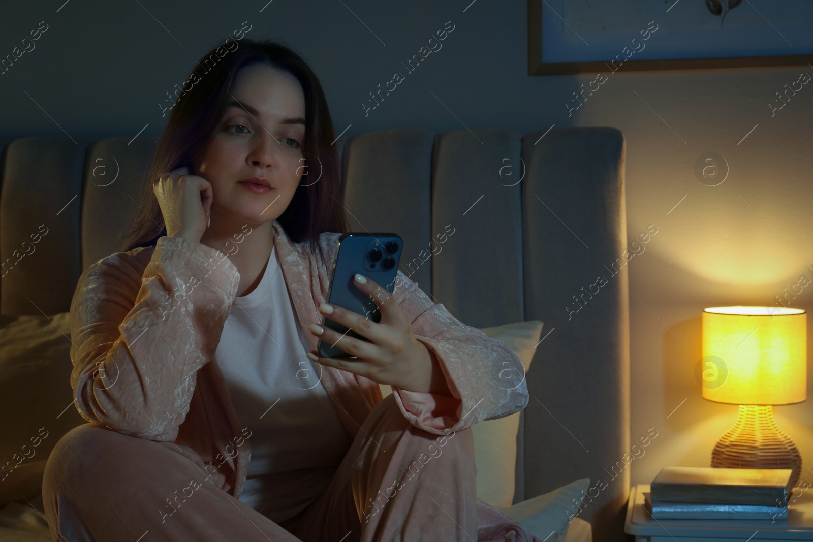 Photo of Woman using smartphone in bedroom at night. Internet addiction