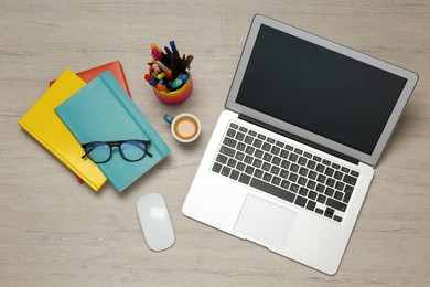 Modern laptop, cup of coffee and office stationery on white wooden table, flat lay. Distance learning