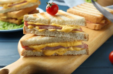 Photo of Tasty sandwiches with ham, melted cheese and tomato on blue wooden table, closeup