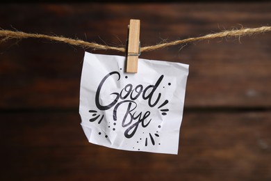 Crumpled paper note with word Goodbye hanging on twine against wooden background 