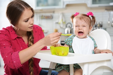 Photo of Mother feeding her little baby with healthy food in kitchen