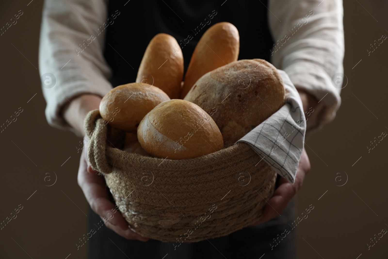 Photo of Man holding wicker basket with different types of bread on brown background, closeup