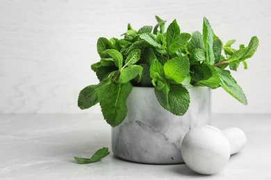 Photo of Marble mortar full of fresh green mint on light background, space for text