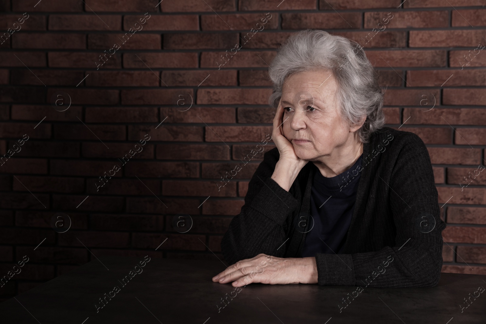 Photo of Poor upset woman sitting at table near brick wall. Space for text
