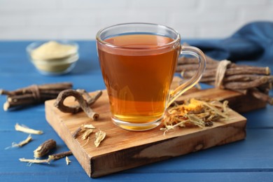 Aromatic licorice tea in cup and dried sticks of licorice root on blue wooden table