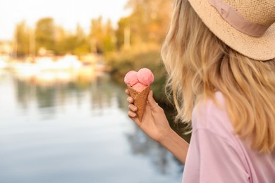 Photo of Young woman with delicious ice cream in waffle cone outdoors, closeup. Space for text