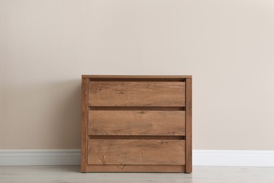 Photo of Wooden chest of drawers near beige wall