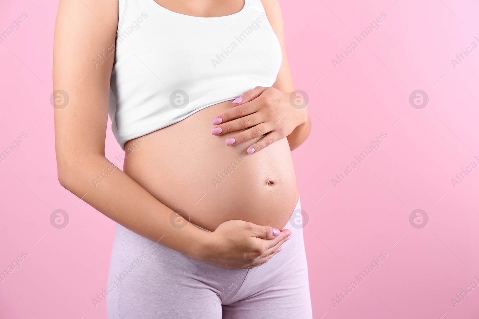 Photo of Young pregnant woman holding hands on belly against color background, closeup. Space for text