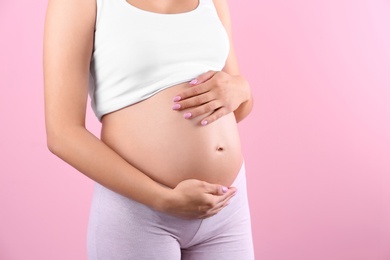 Photo of Young pregnant woman holding hands on belly against color background, closeup. Space for text