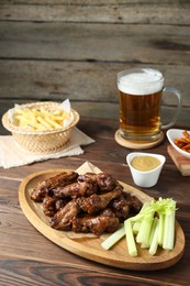 Delicious chicken wings served with beer on wooden table