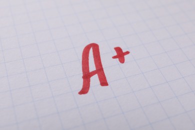 School grade. Red letter A with plus symbol on notebook paper, closeup