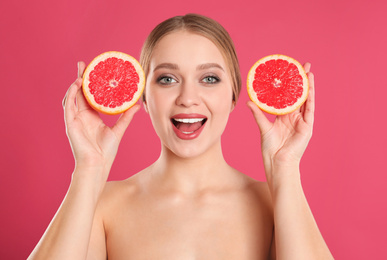 Young woman with cut grapefruit on pink background. Vitamin rich food